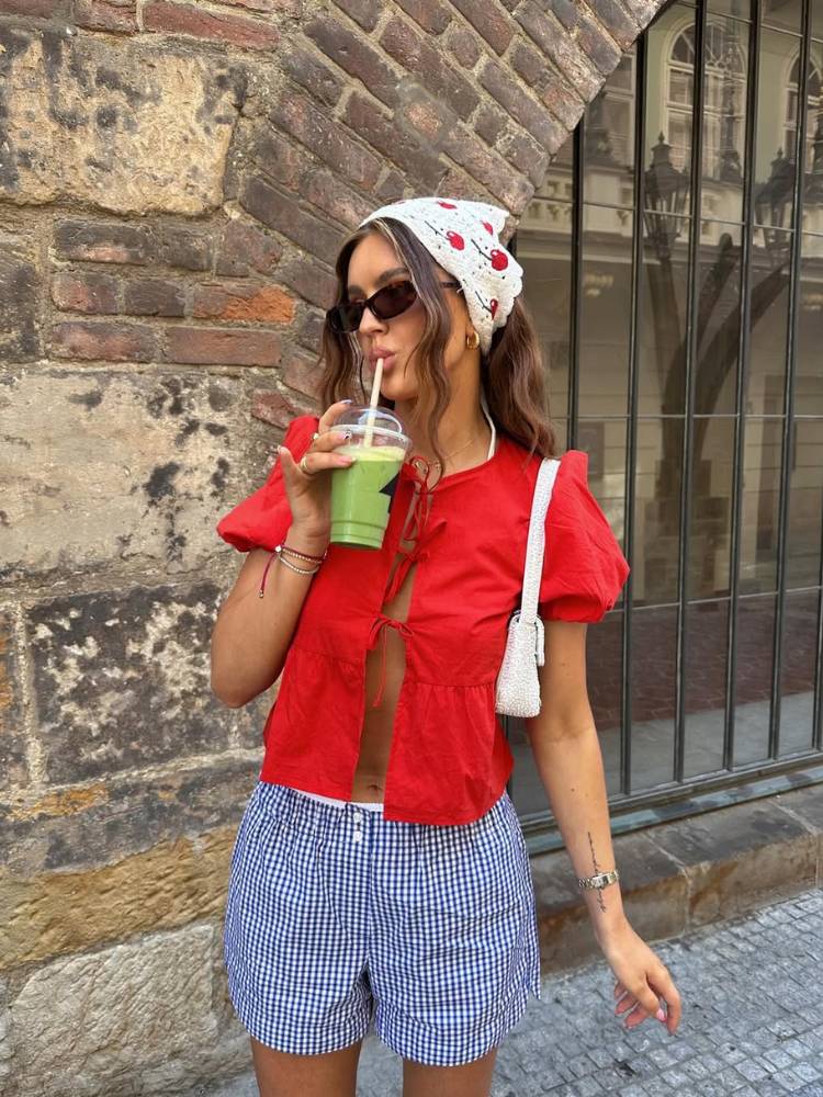 Mulher d epele clara usando bandana, blusa vermelha de amarração e shorts branco e azul 