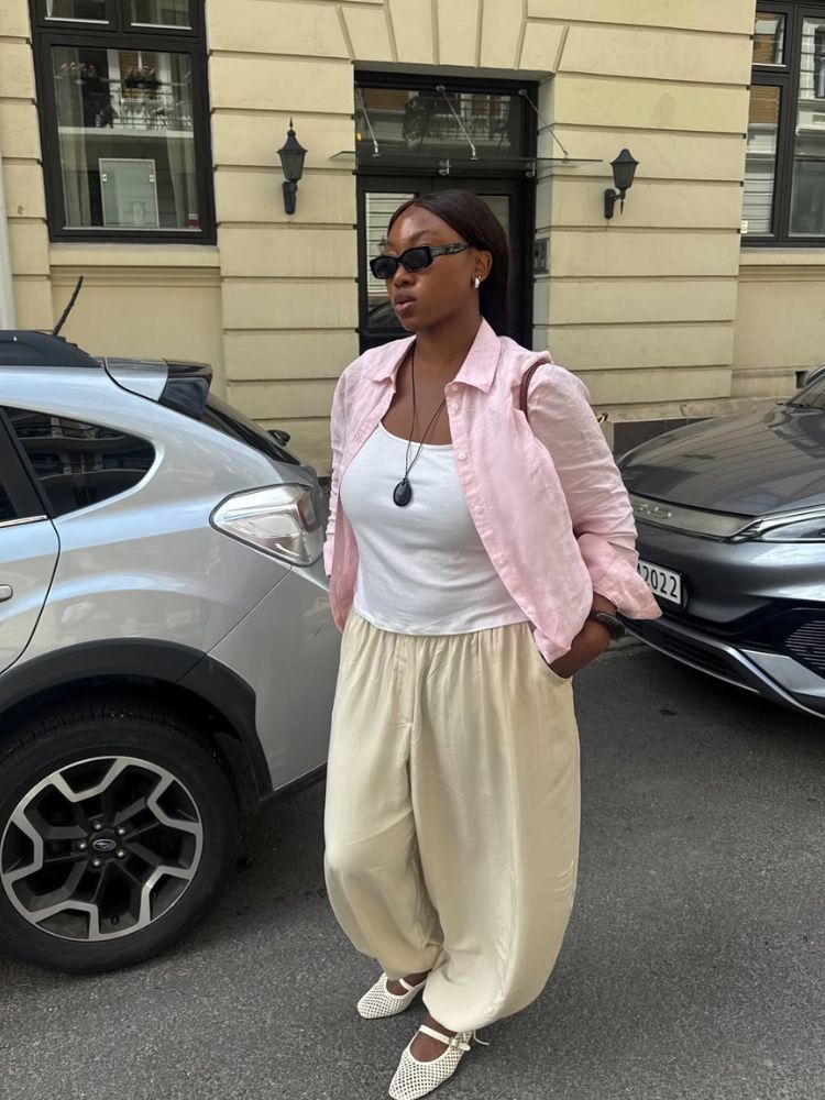Mulher de pele negra usando camisa leve rosa clara, regata branca, calça leve amarelo-manteiga