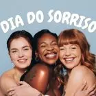 Mulheres sorrindo se abraçando e frase: Dia do Sorriso