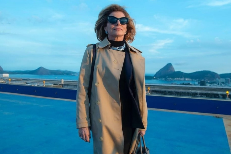 Foto do estilo de Odete Roitman em Vale Tudo: blusa preta, colar prata e sobretudo Burberry cáqui