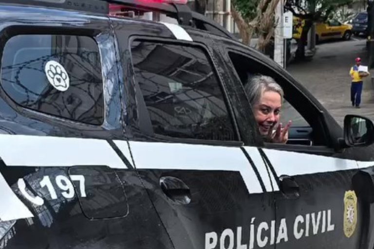 Carro da Polícia Civil do Rio Grande do Sul estacionado em via urbana, com sirene ligada. Veículo preto e branco, identificado pelo número 197, exibe adesivos institucionais. No banco do motorista, uma pessoa aparece sorrindo e acenando.
