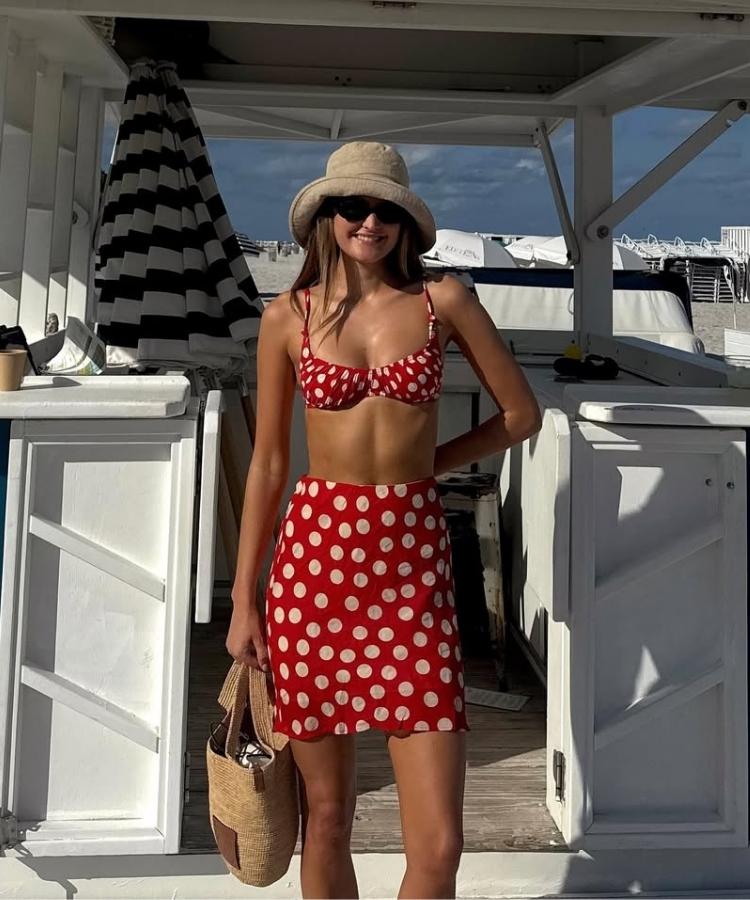 Foto de mulher usando chapéu de crochê, óculos de sol, bolsa de palha, biquíni e saia de bolinhas vermelho e branco