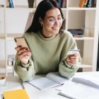 Mulher usando celular e cartão de crédito em casa enquanto compara opções de cartão sem anuidade em 2026.