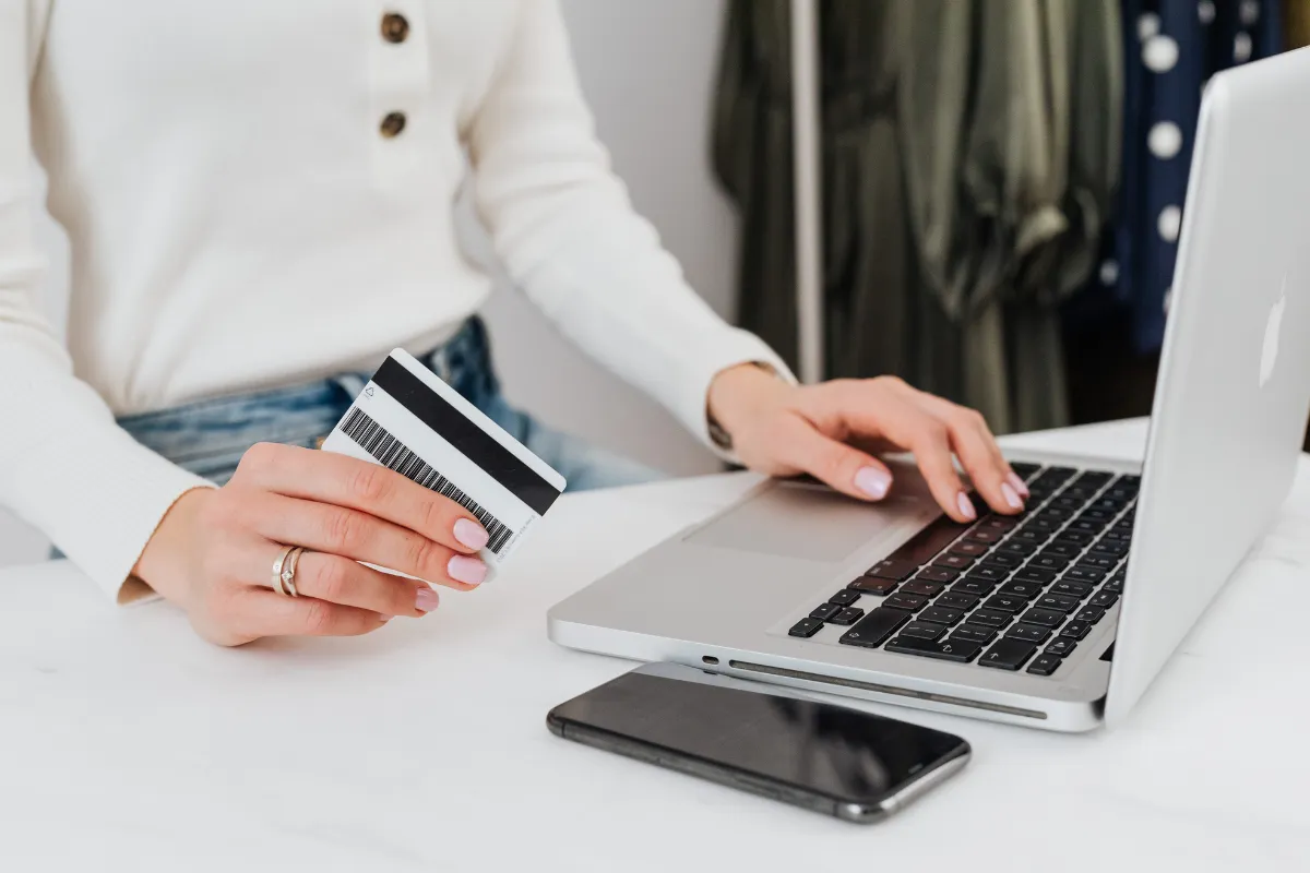 Pessoa segurando cartão bancário enquanto utiliza notebook para contratar serviço financeiro online com segurança.