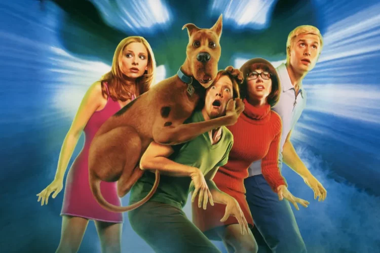 Turma do Scooby-Doo em versão live-action reunida durante investigação sobrenatural em cenário iluminado.