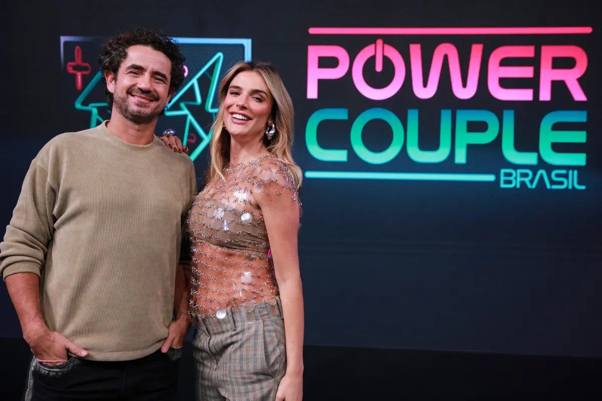 Casal posando em frente ao painel do reality Power Couple Brasil durante divulgação oficial do programa