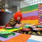 Foto de Yayoi Kusama de cabelo vermelho sentada em uma mesa pintando