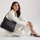 Modelo usando look branco e segurando bolsa de couro média preta da Move & Co