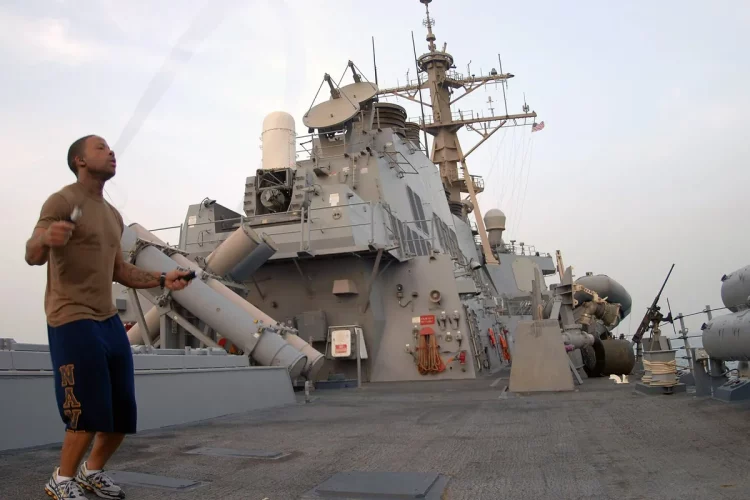 Marinheiro pulando corda com roupa esportiva no convés de um navio, ao ar livre