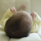 Bebê deitado de costas sobre lençol claro, com a cabeça e os pezinhos à mostra.