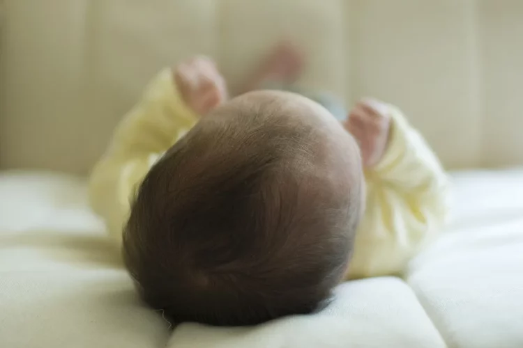Bebê deitado de costas sobre lençol claro, com a cabeça e os pezinhos à mostra.